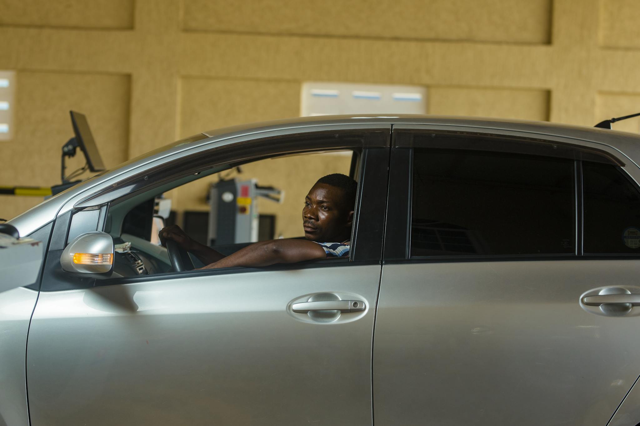 A man sits in a car during a vehicle inspection in a garage setting.